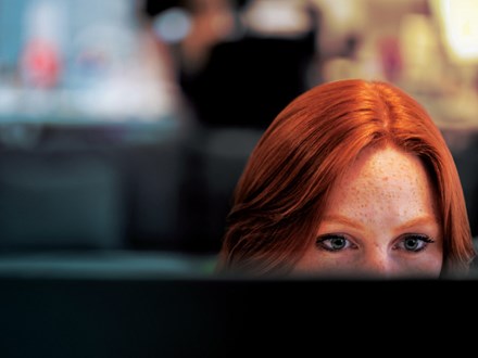 Red haired woman half hidden behind her screen at work. 